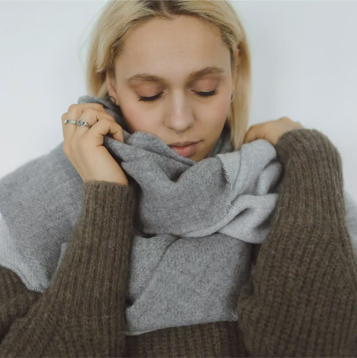 Blondwłosa kobieta z zamkniętymi oczami obejmuje szyję szalem.