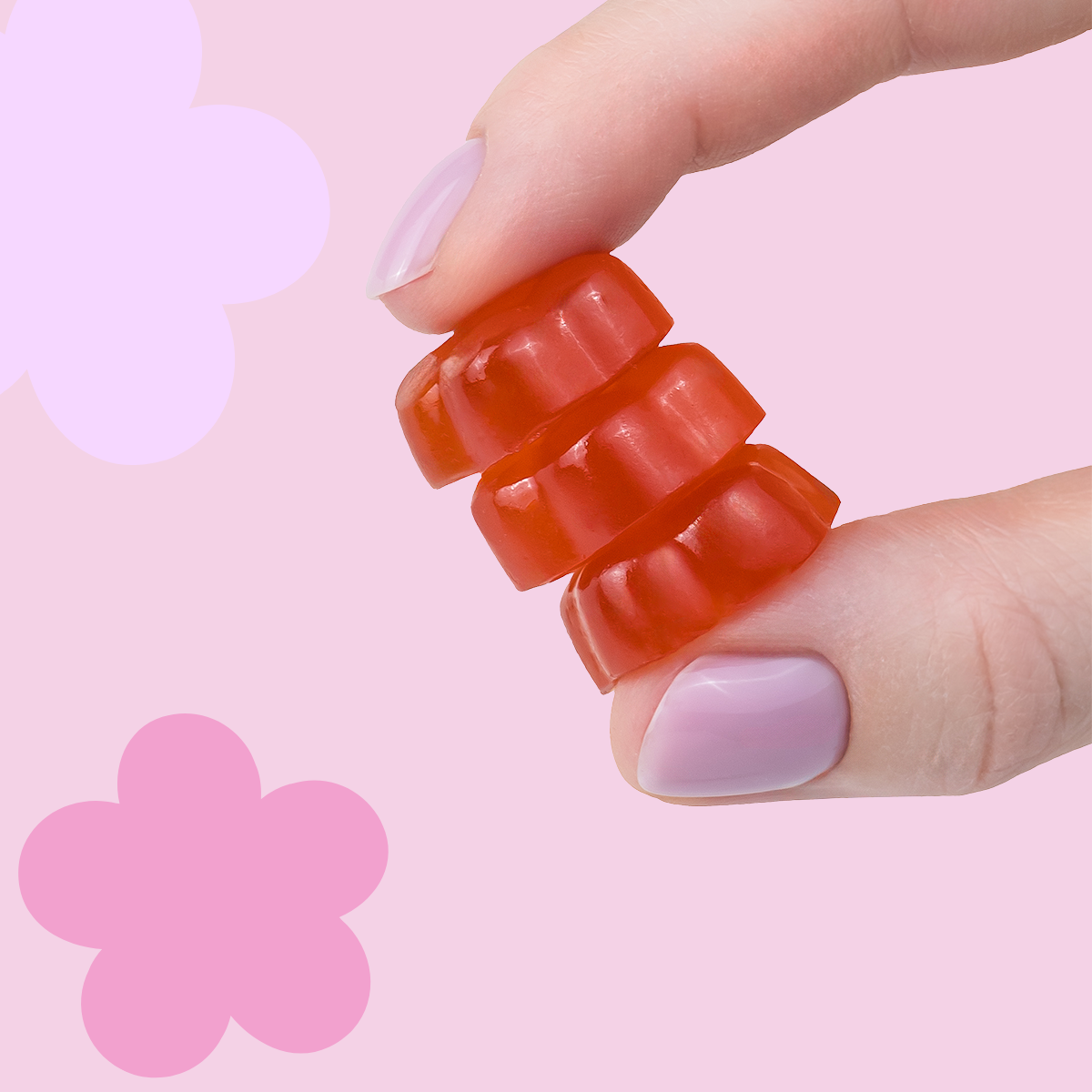 Wegańskie żelki so bloomy w kształcie kwiatów trzymane w dłoni na różowym tle