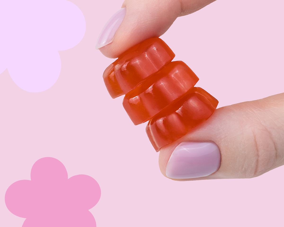 Wegańskie żelki so bloomy w kształcie kwiatów trzymane w dłoni na różowym tle