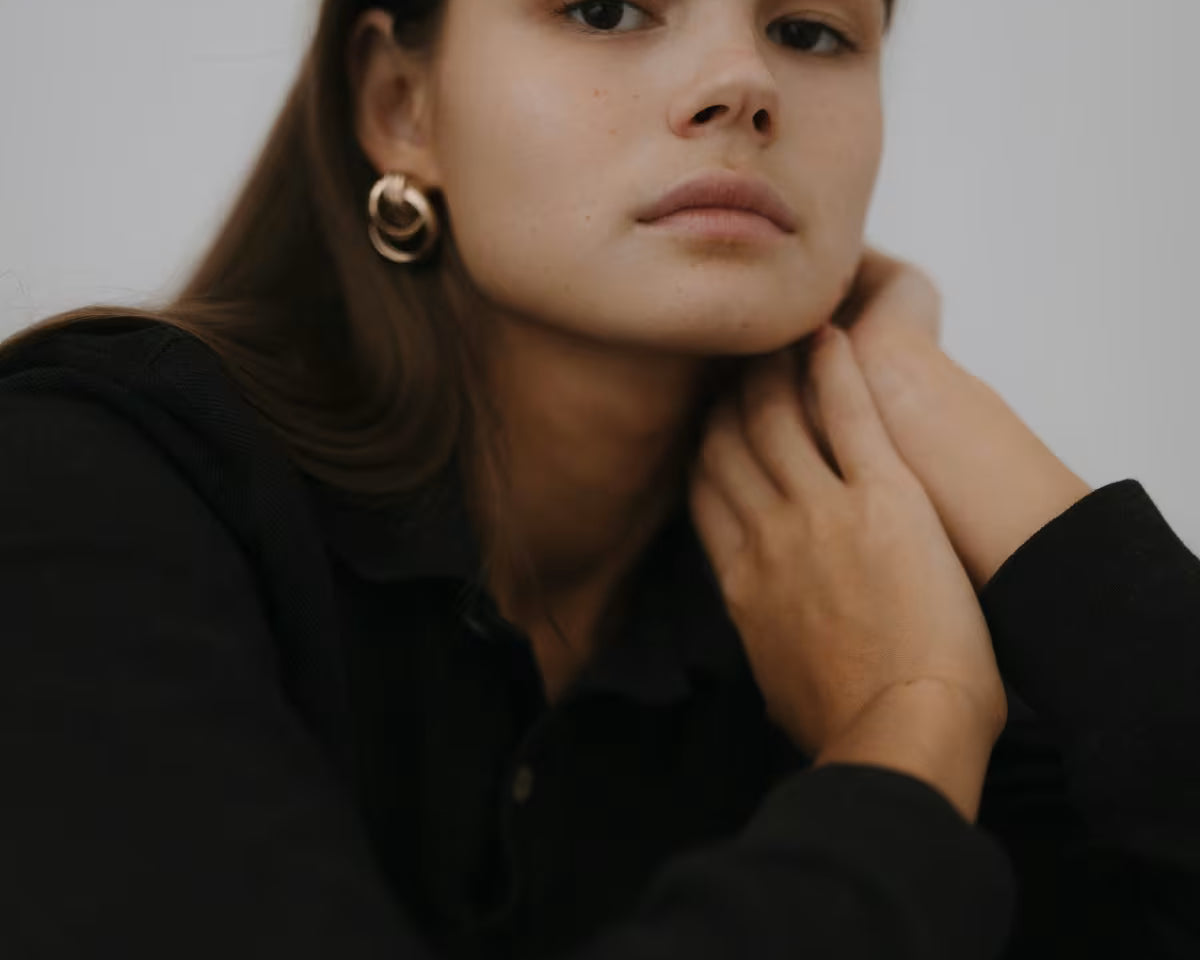 Dziewczyna z gładką cerą i długimi włosami patrzy się w obiektyw trzymając dłonie pod twarzą. 