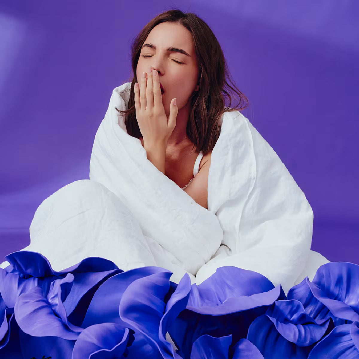 Dziewczyna z brązowymi włosami owinięta białą pościelą ziewa zasłaniając usta dłonią. Otoczona jest fioletowym tłem i fioletowymi kwiatami.