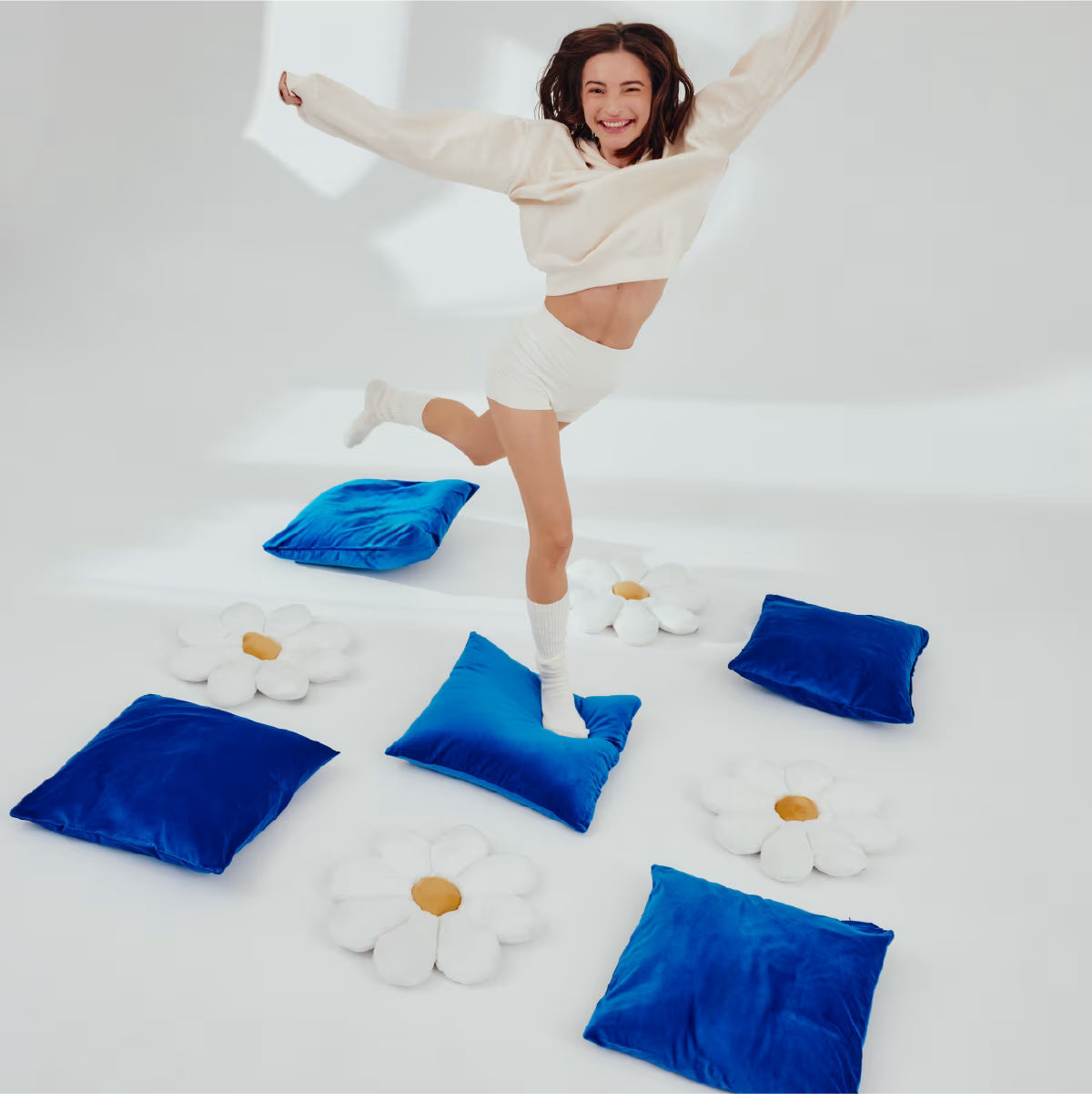 Uśmiechnięta dziewczyna skacze po niebieskich poduszkach ułożonych naprzemiennie z poduszkami w kształcie stokrotek