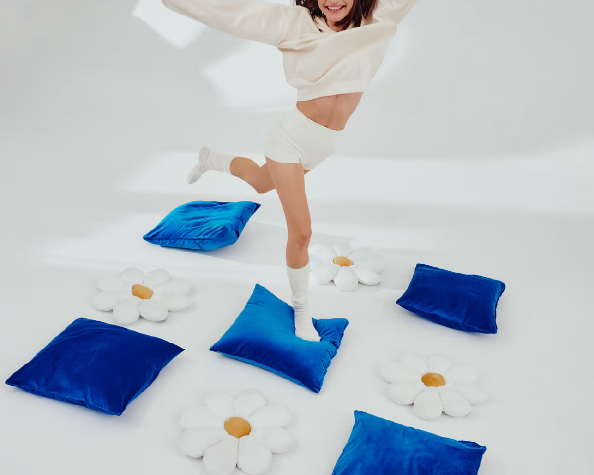 Uśmiechnięta dziewczyna skacze po niebieskich poduszkach ułożonych naprzemiennie z poduszkami w kształcie stokrotek