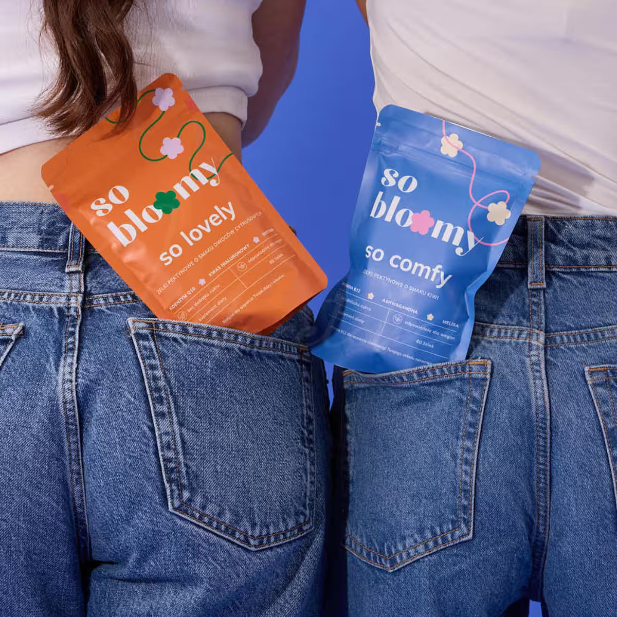 Dwie osoby stoją tyłem do kamery, mają ubrane jeansy i białe koszulki. W kieszeniach jeansów znajdują się paczki żelek funkcjonalnych so bloomy - żelki so lovely i so comfy.