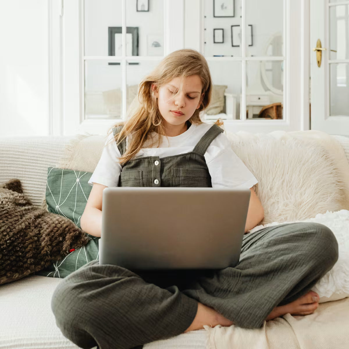 Zmęczona dziewczyna w blond włosach siedzi na kanapie i pracuje na laptopie