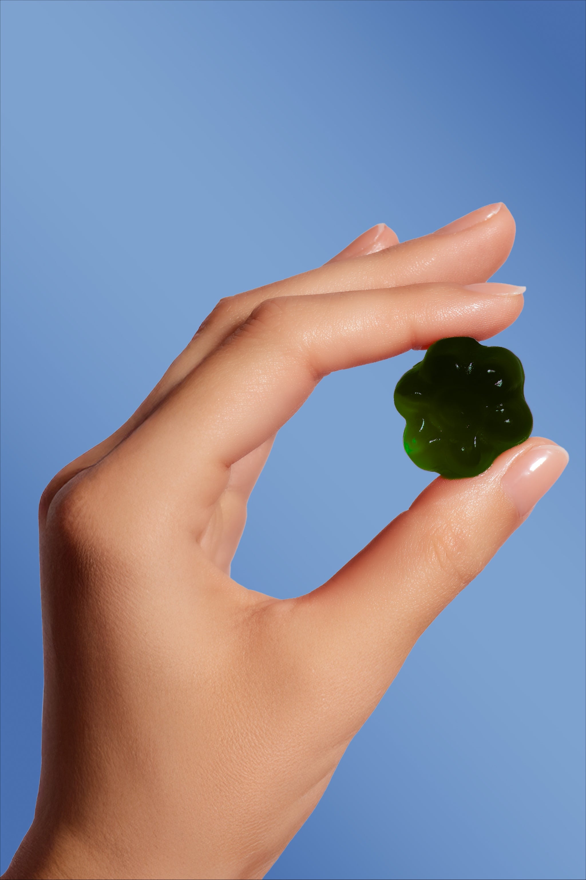 Dłoń na niebieskim tle trzymająca żelka so comfy w kształcie kwiatka