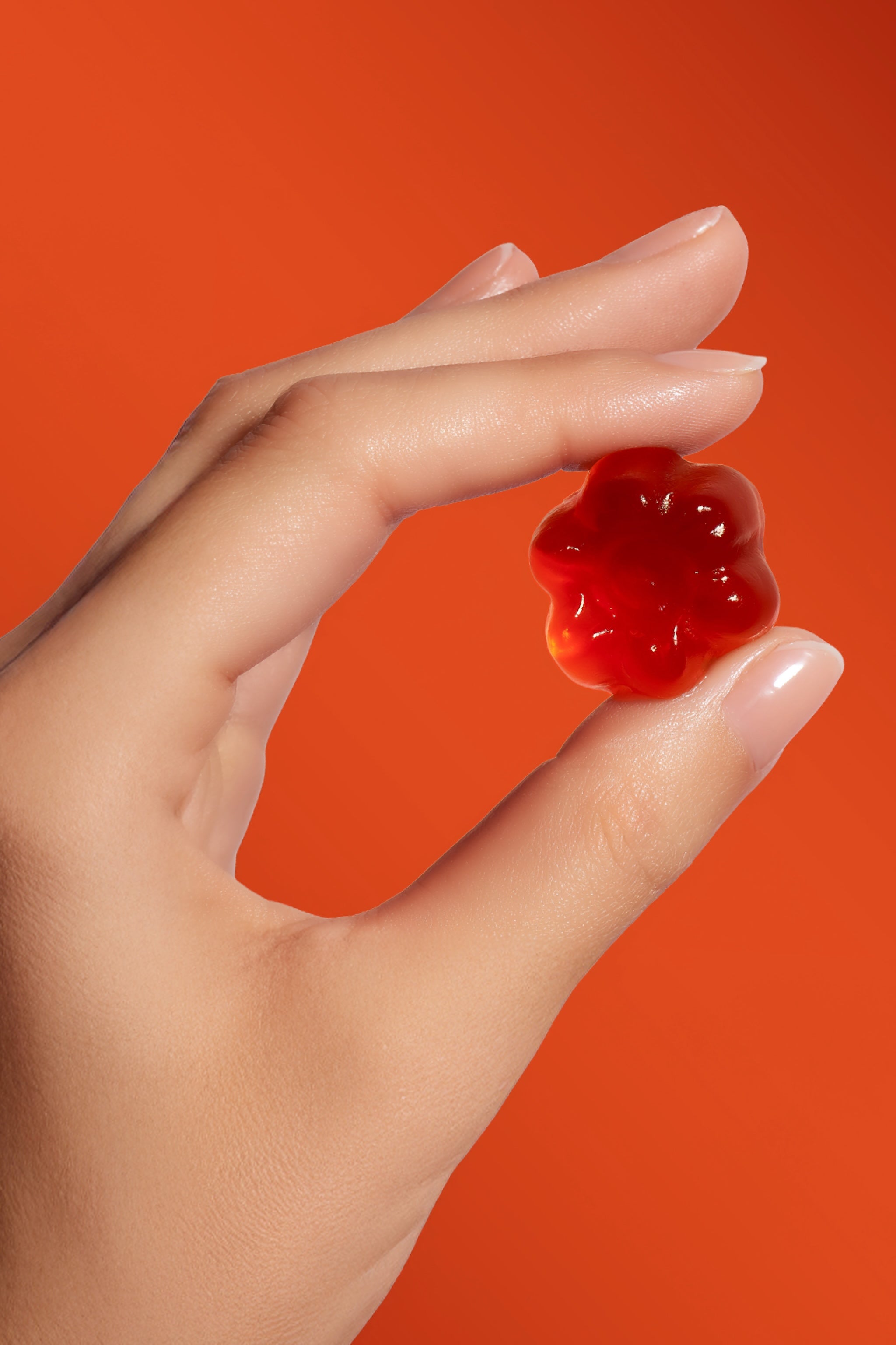 Dłoń trzymająca pomarańczowego żelka so lovely w kształcie kwiatka