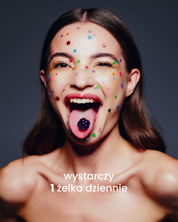 Dziewczyna z przyklejonymi małymi kolorowymi kwiatkami na twarzy wystawia język, na którym jest fioletowa żelka so bloomy. Poniżej napis: wystarczy 1 żelka dziennie.