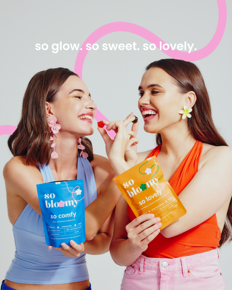 Dwie uśmiechnięte dziewczyny jedzą wegańskie żelki so bloomy. Jedna z nich trzyma opakowanie żelek so comfy, druga trzyma opakowanie so lovely.